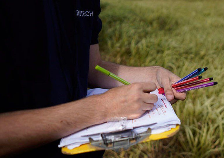 Caucasian man in a navy blue Arbtech-branded polo shirt holding a note pad and multicoloured pens in a field